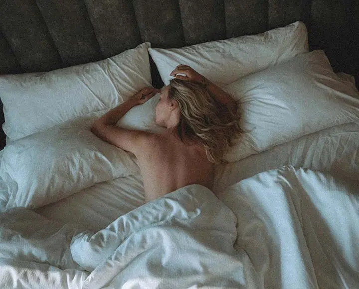 Woman sleeping peacefully in a cool, dark bedroom with soft neutral bedding