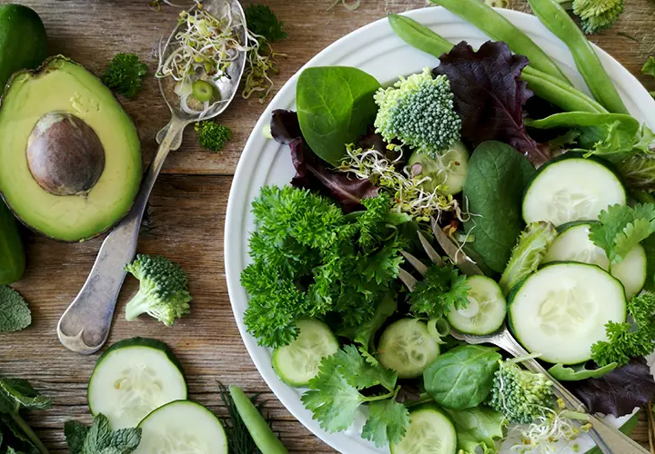Plate of fiber-rich vegetables with avocado, broccoli, cucumber, greens, and sprouts