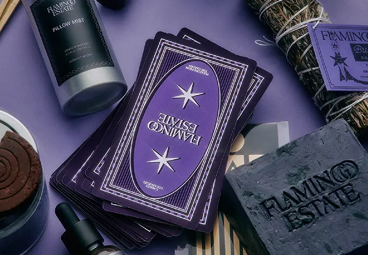 Flamingo Estate oracle cards with pillow mist, ritual incense and botanical products arranged on a purple surface