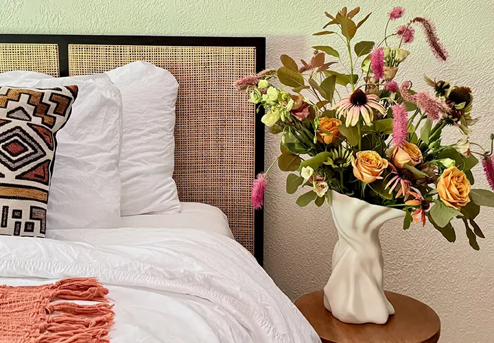 Sullivan Owen porcelain vase with a colorful floral arrangement beside a bed