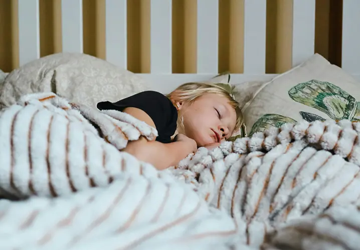 Young child sleeping in bed under a blanket