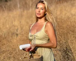 Jesse Golden, founder of The Golden Secrets, wearing a yellow dress and holding a skincare product outdoors.