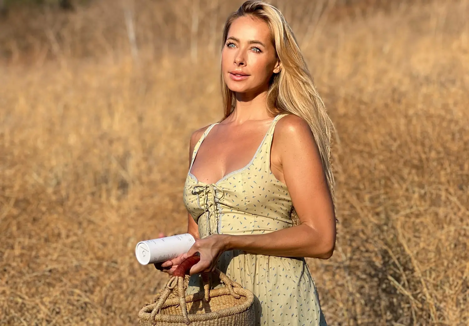 Jesse Golden, founder of The Golden Secrets, wearing a yellow dress and holding a skincare product outdoors.